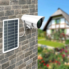 Outdoor portable mini solar charger panel mounted on brick wall powering a security camera outdoors