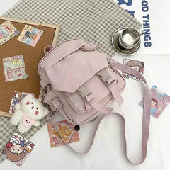 Light pink Korean Nylon Oxford Fabric Versatile Literature Backpack with bear pendant on a checkered cloth background.