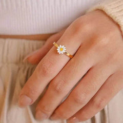 Fidget spinner rotatable ring for women with a gold band and white flower design worn on a finger