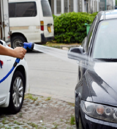 Flexible garden hose spraying water to wash a car outdoors with a blue nozzle and adjustable spray pattern.