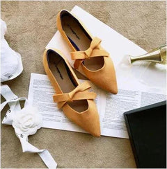 Yellow flat casual boat shoes with bow in Mary Jane style placed on open book with decorative white flower and box nearby