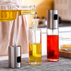 Kitchen condiment bottle with stainless steel spray head being filled with oil, next to a filled bottle with red liquid on kitchen countertop