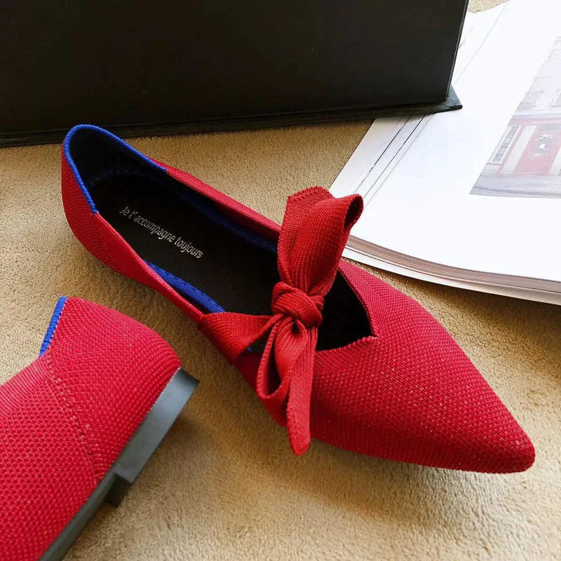 Red flat casual boat shoe with bow detail and pointed toe design on beige surface