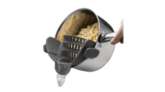 Hand holding pot with grey silicone pot strainer attached, draining water from cooked pasta
