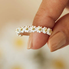 Close-up of a women's fidget spinner rotatable metal ring with a delicate white and gold flower design held between fingers.