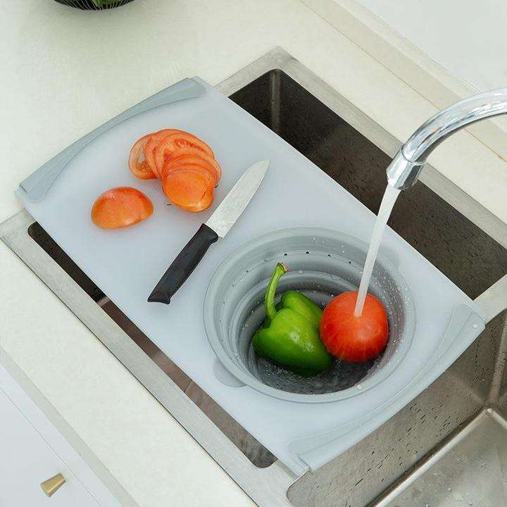 Kitchen plastic chopping board with silicone drainage basin, used for cutting vegetables over a sink.