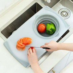 Kitchen plastic chopping board with integrated silicone drainage basin, slicing tomatoes and green bell pepper over kitchen sink.