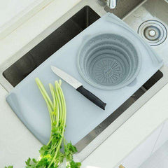 Gray kitchen plastic chopping board with silicone drainage basin, knife, and fresh celery over kitchen sink