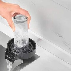 Hand using automatic glass cup washer to clean an inverted glass cup under high pressure water flow on kitchen sink accessory