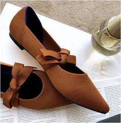 Brown flat casual boat shoes with bow detail and pointed Mary Jane style design on white surface next to a glass bottle