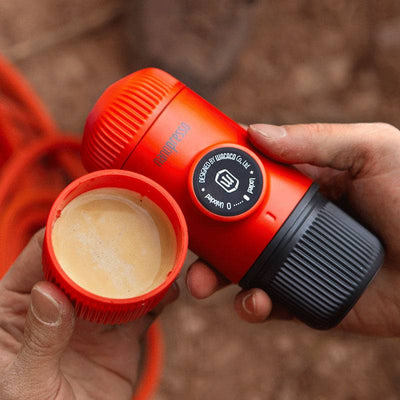 Portable compact electric espresso coffee maker with cup held in hands outdoors