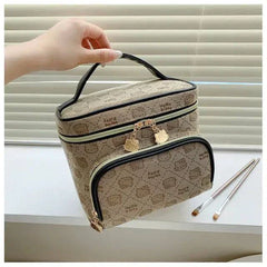 Hello Kitty makeup bag with brown patterned design, black handle, and gold zipper pulls, held by a hand near makeup brushes on a white surface.