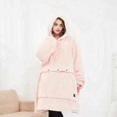 Woman wearing a soft pink oversized heated hoodie blanket with hood and front pocket indoors