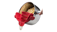 Red silicone pot strainer clipping onto a saucepan to drain water from cooked pasta.