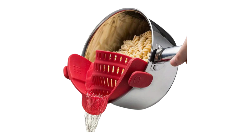 Red silicone pot strainer clipping onto a saucepan to drain water from cooked pasta.