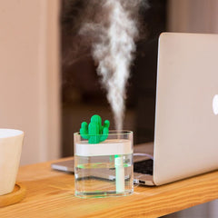 Compact ultrasonic air humidifier releasing fine mist on desk next to laptop