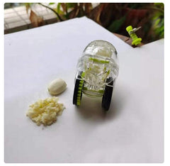 Transparent rolling garlic chopper with black wheels next to a peeled garlic clove and minced garlic on a white surface
