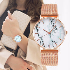 Rose gold mesh band watch with minimalist marble dial on wrist and matching clutch purse